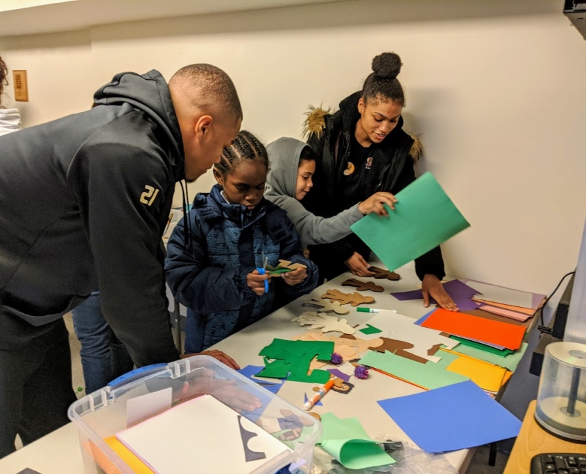 Two student volunteers with JMU CMSS help children cut out and make paper people