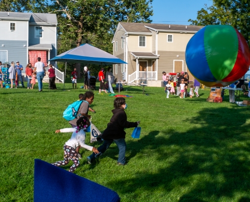 Children chase a large beach ball in the foreground as families mingle with community partners in the back.